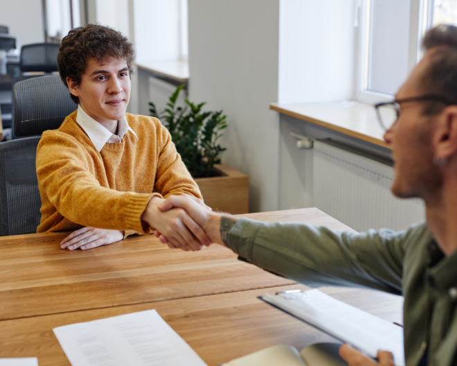 A successful interview moment as two individuals shake hands across the table, signaling a positive outcome in a professional setting.